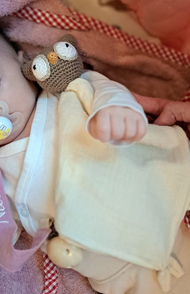 Neugeborenes Baby hält personalisiertes Schmusetuch mit gehäkelter Eule aus weichem Musselin im Kinderwagen, liebevolles Geschenk zur Geburt.